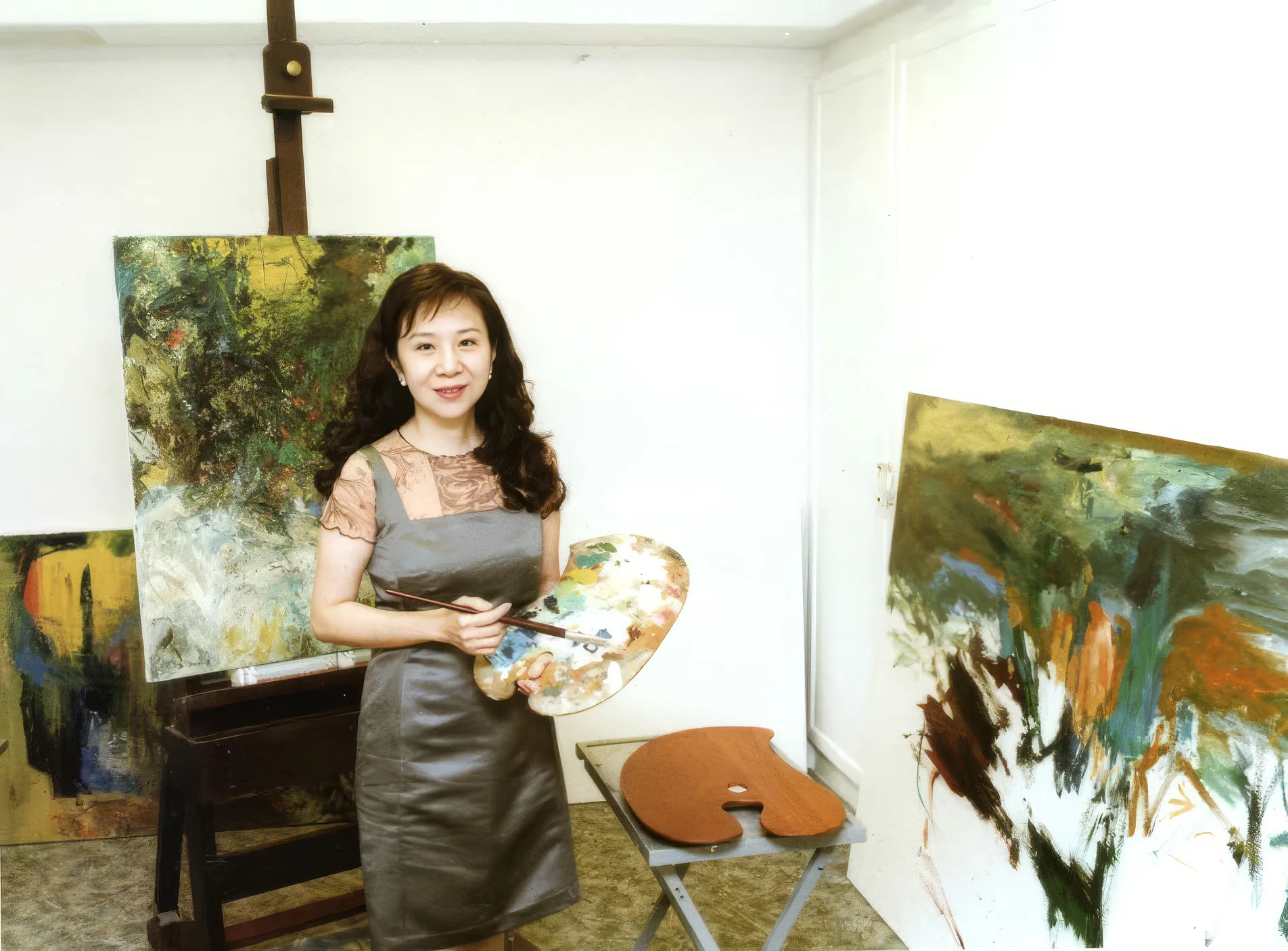 侯翠杏站在畫室裡，手持調色盤與畫筆，身後是兩幅大尺幅抽象油畫。